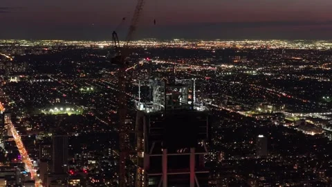 Construction crane operating on top of rising skyscraper at night revealing urba Stock Footage 335226328