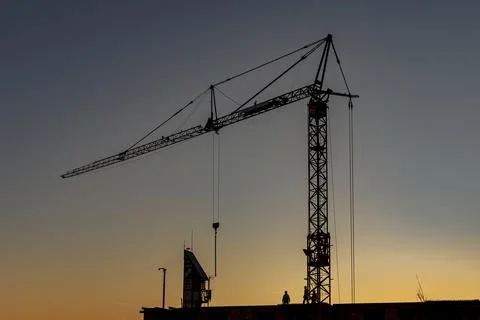 Construction Crane Silhouette at Sunset with Workers on Building Site Stock Photos