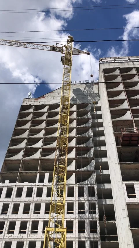 A construction crane stands next to an unfinished high-rise under a clear sky. Stock-Footage 341683211
