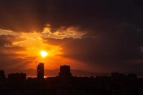 Construction crane at sunset on a background of orange sun, a city by the sea Stock Photos