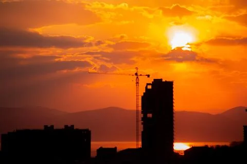 Construction crane at sunset on a background of orange sun, a city by the sea Stock Photos