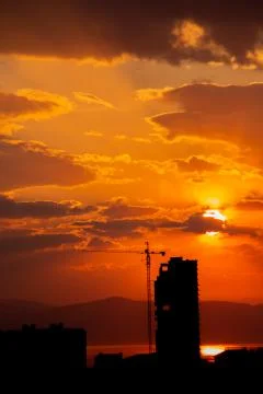 Construction crane at sunset on a background of orange sun, a city by the sea Stock Photos