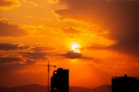 Construction crane at sunset on a background of orange sun, a city by the sea Foto stock