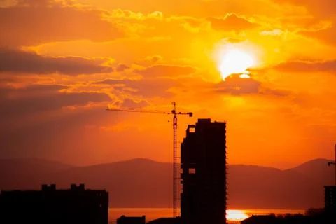 Construction crane at sunset on a background of orange sun, a city by the sea Stock Photos