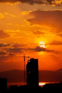 Construction crane at sunset on a background of orange sun, a city by the sea 写真素材