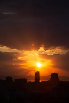 Construction crane at sunset on a background of orange sun, a city by the sea 写真素材