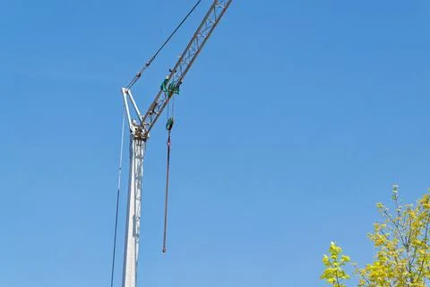 Construction crane tower with hook and chain against clear blue sky and tree Stock Photos