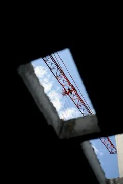 Construction crane visible through a gap in a concrete wall against blue sky Stock Photos