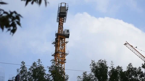 A construction crane works against a background of blue and green trees. The Stock Footage 114687849
