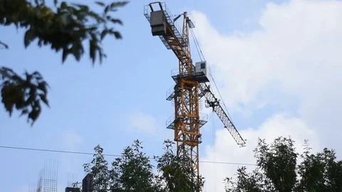 A construction crane works against a background of blue sky and green trees. The Stock Footage 114687854