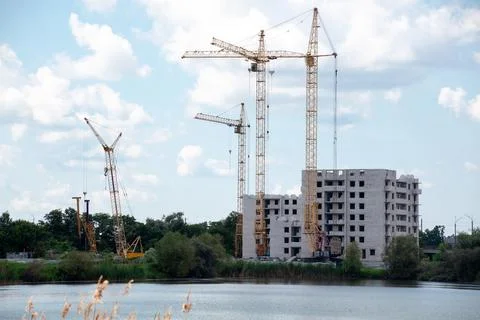 Construction cranes and building on construction site with cloudy blue sky Stock Photos