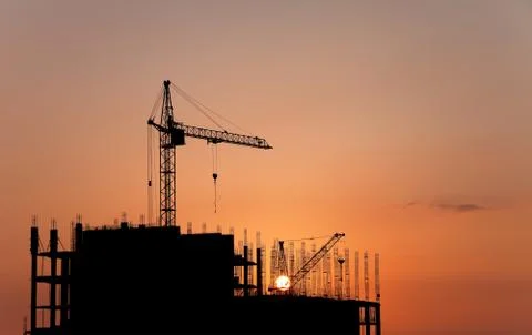 Construction cranes and concrete structure at sunset Stock Photos