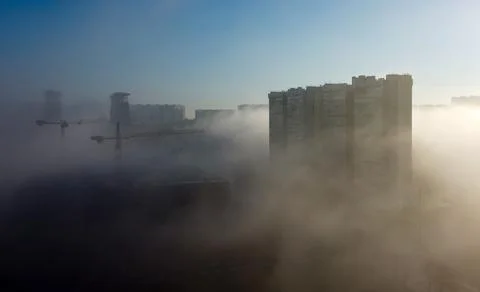 Construction cranes and a multi-storey residential building, shrouded in fog, Stock Photos