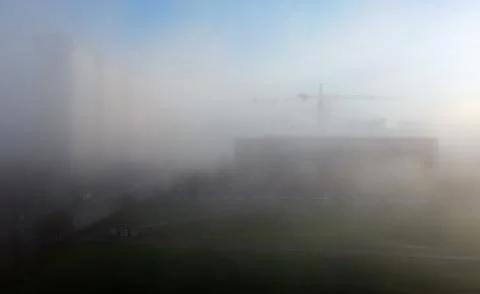 Construction cranes and a multi-storey residential building, shrouded in fog, Stock Photos