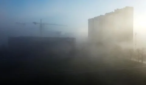 Construction cranes and a multi-storey residential building, shrouded in fog, Stock Photos