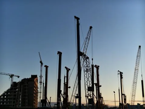 Construction cranes and piling rigs silhouetted against clear evening sky over Stock Photos