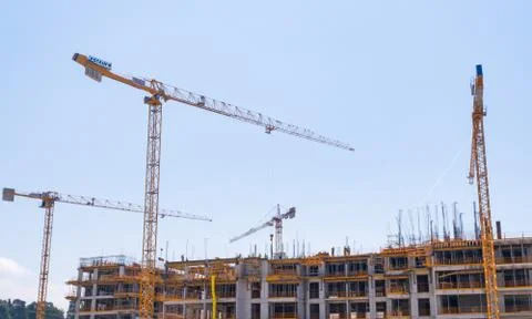 Construction cranes on the background of a building under construction with w Stock Photos