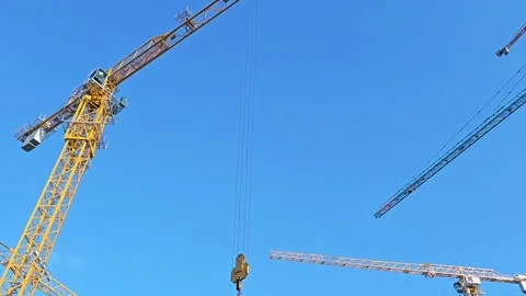 Construction cranes with extended arms and lifting hooks against blue sky Stock Footage 297615224