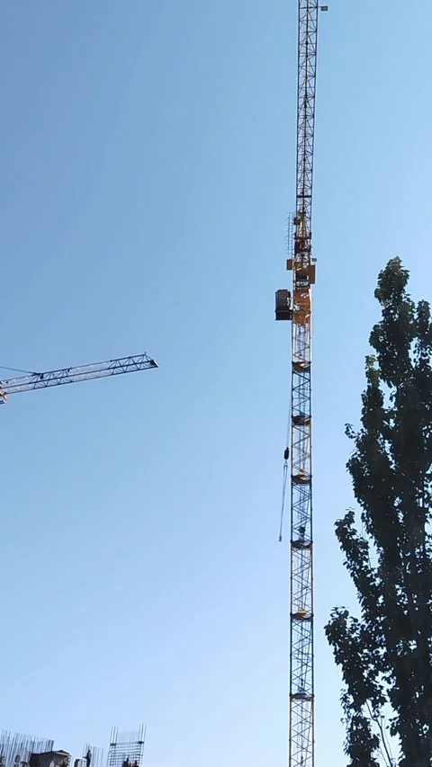 Construction cranes lifting materials against clear blue sky with trees in Stock Footage 340606605