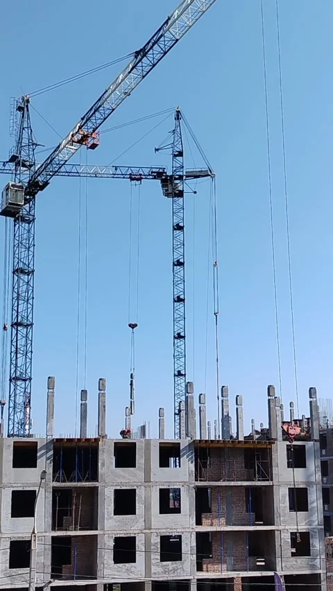 Construction cranes lifting materials at building site under clear blue sky Stock Footage 340606813