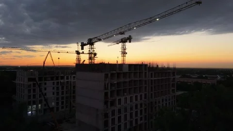 Construction cranes lifting materials at sunset over building site Stock Footage 339124431