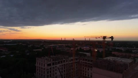 Construction cranes operate at sunset over urban landscape with clouds Stock Footage 339124095