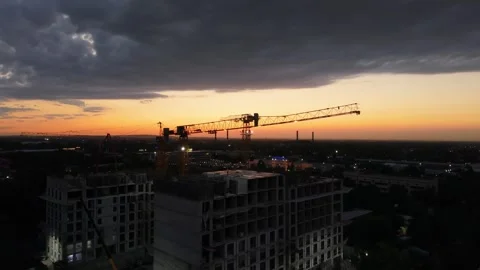 Construction cranes operate at sunset over urban skyline, clouds above Stock Footage 339124503