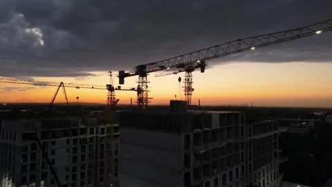Construction cranes operate at sunset over urban skyline, dramatic clouds Stock Footage 339124565