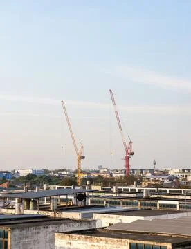 Construction cranes over city rooftops. Stock Photos