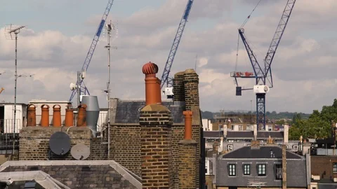 Construction cranes raise amongst chimneys and smokestacks of residential London Stock Footage 97303050