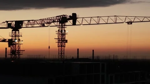 Construction cranes silhouetted against sunset sky, urban skyline visible Stock Footage 339124605