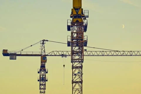 Construction cranes at sunset time with crescent moon in the sky Stock Photos