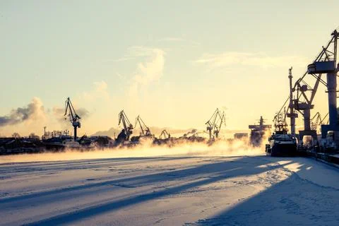 Construction cranes in white background, deep sunset shadows on frozen river Stock Photos