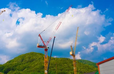 Construction cranes work on creation site against blue sky and mountains Stock Photos