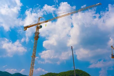 Construction cranes work on creation site against blue sky background. Stock Photos