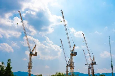 Construction cranes work on creation site against blue sky background. Stock Photos