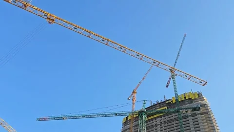 Construction cranes working on a high-rise building against a clear blue sky Stock Footage 297615279
