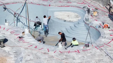 Construction crew applies pebble sheen finish inside curved pool, one worker Stock Footage 339151315