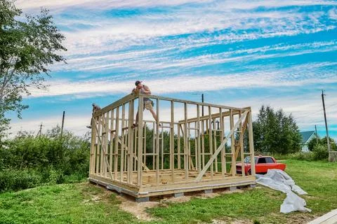 Construction crew builds frame house on foundation made of concrete blocks. Stock Photos