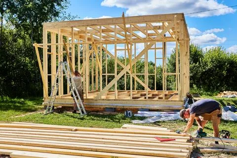 Construction crew of two workers builds timber frame as one cuts boards wit.. Stock Photos