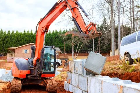 Construction crew uses an excavator to place concrete blocks on building site Stock Photos