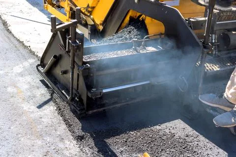 Construction crew works with paving machine to lay asphalt on new road project Stock Photos
