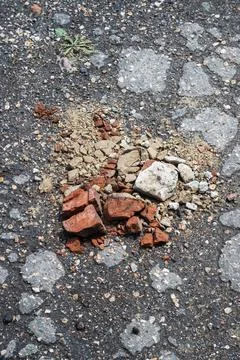 Construction debris and broken bricks scattered on rough asphalt surface Stock Photos