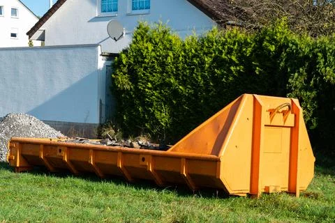 Construction debris container placed in a grassy area near buildings Stock Photos