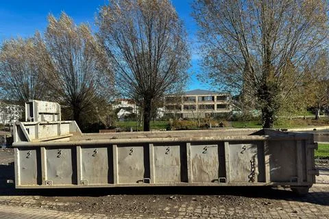 Construction debris container situated in a city park during the day Stock Photos