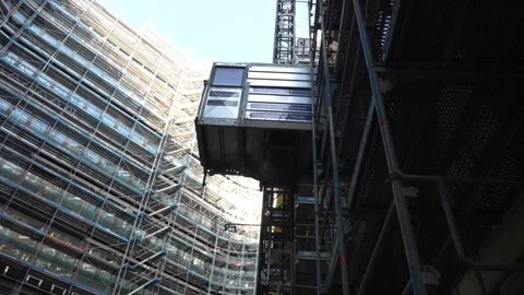 Construction elevator descending along scaffolding on modern building facade Vídeos de archivo 332811539