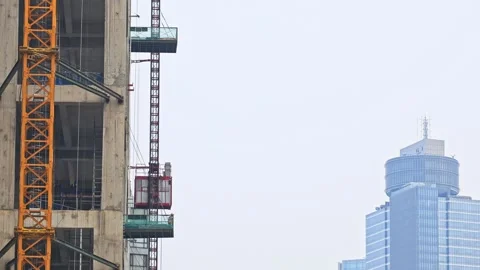 Construction elevator moving down concrete skyscraper next to completed glass Stock Footage 337974954