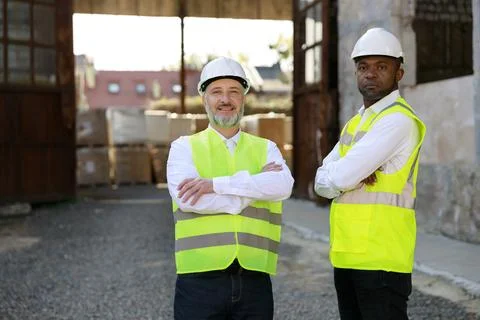 Construction engineer and foreman standing together, crossing hands on building Stock Photos