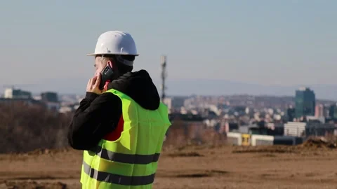 Construction engineer in hard hat and safety vest talking on smartphone at Stock Footage 330121538
