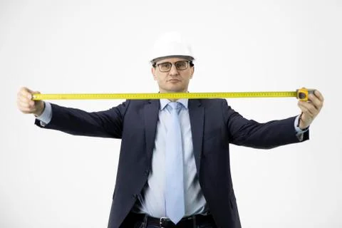Construction engineer in hard hat holds measuring tape seriously looks at camera Stock Photos